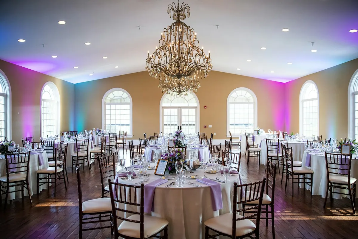 A banquet room set with round tables under a chandelier
